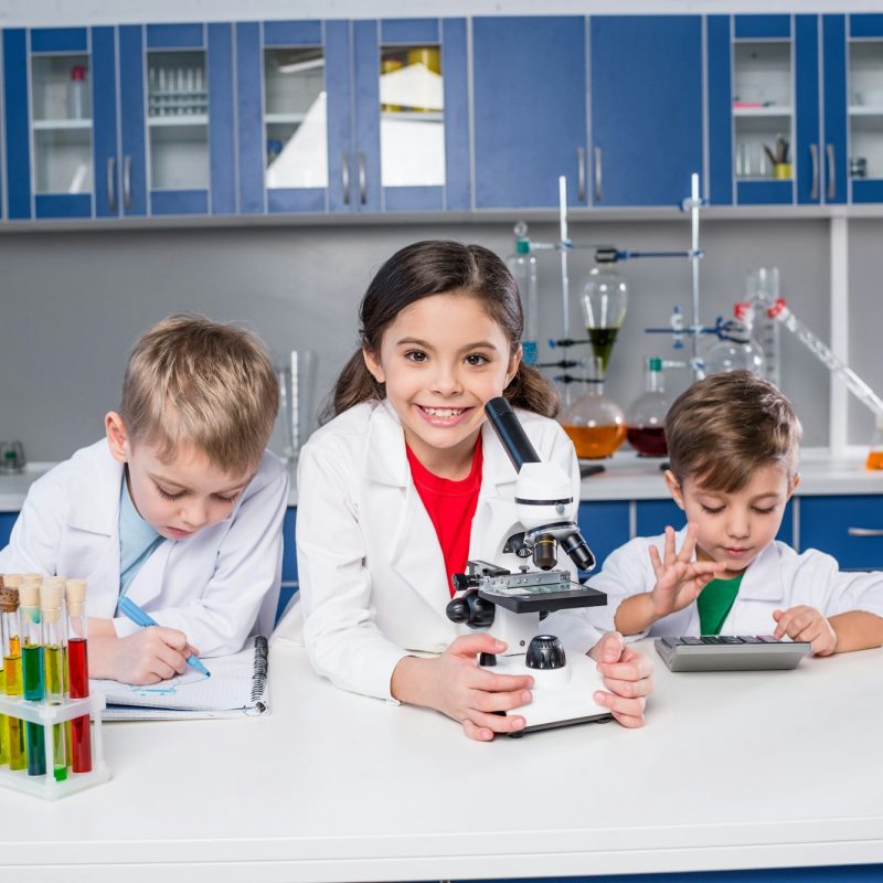 three-kids-in-chemical-laboratory-making-notes-and-using-microscope-and-calculator.jpg